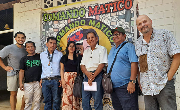 Eine Gruppe von sieben Personen steht vor einer Hauswand mit dem Logo von Comando Matico